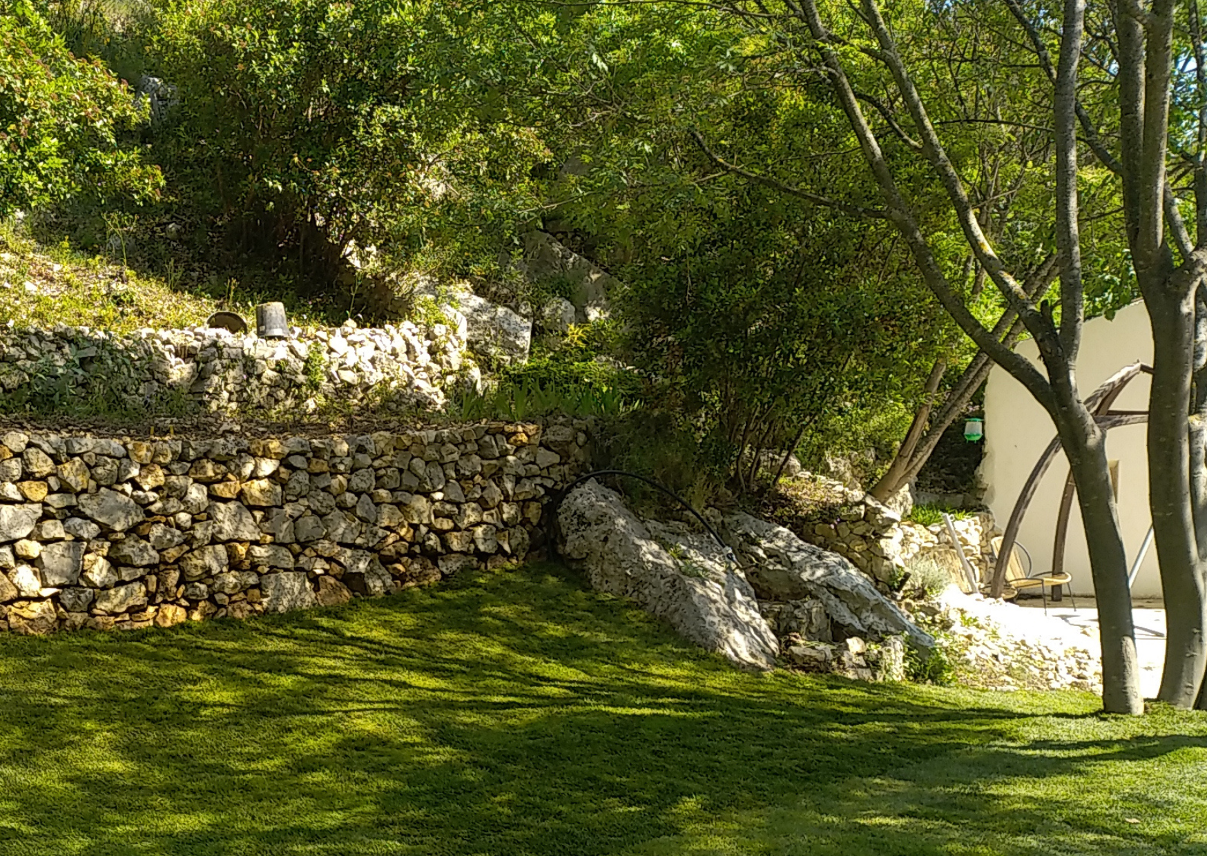 Mur en pierre sèche intégré dans un jardin paysager avec pelouse et végétation naturelle