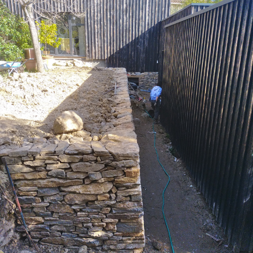 Construction d’un mur de soutènement en pierre sèche sur terrain en pente lors d’un aménagement extérieur